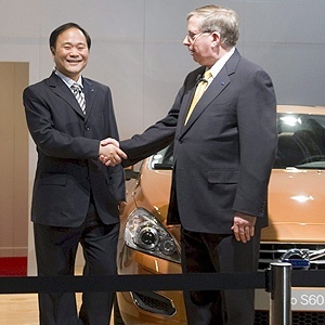 Li Shufu, pela Geely, e Lewis Booth, pela Ford, cumprimentam-se neste domingo em Gotemburgo, na Suécia, no anúncio da venda da Volvo à empresa chinesa; atrás deles, um exemplar do sedã S60, renovado pela Volvo este ano